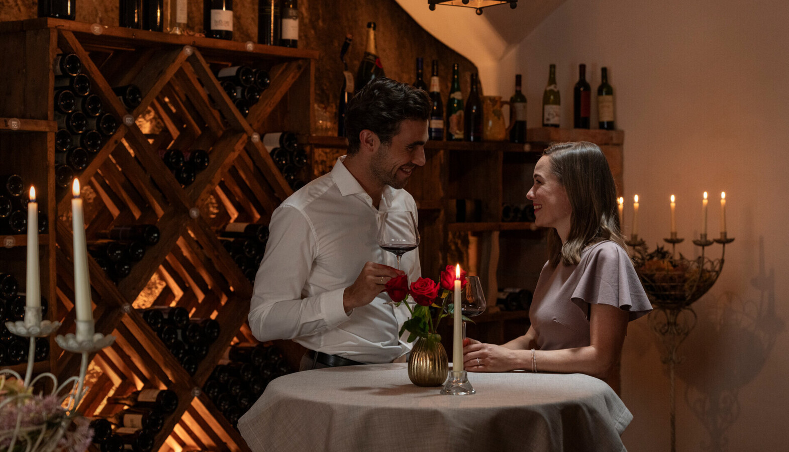 Perfekter Urlaub für Paare am Fuschlsee - Pärchen mit Weingläsern, rote Rosen und Kerze am Tisch.